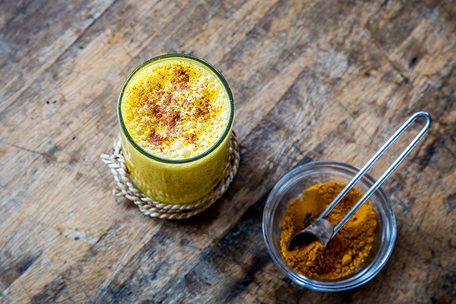 A glass of yellow liquid next to a bowl of curry.