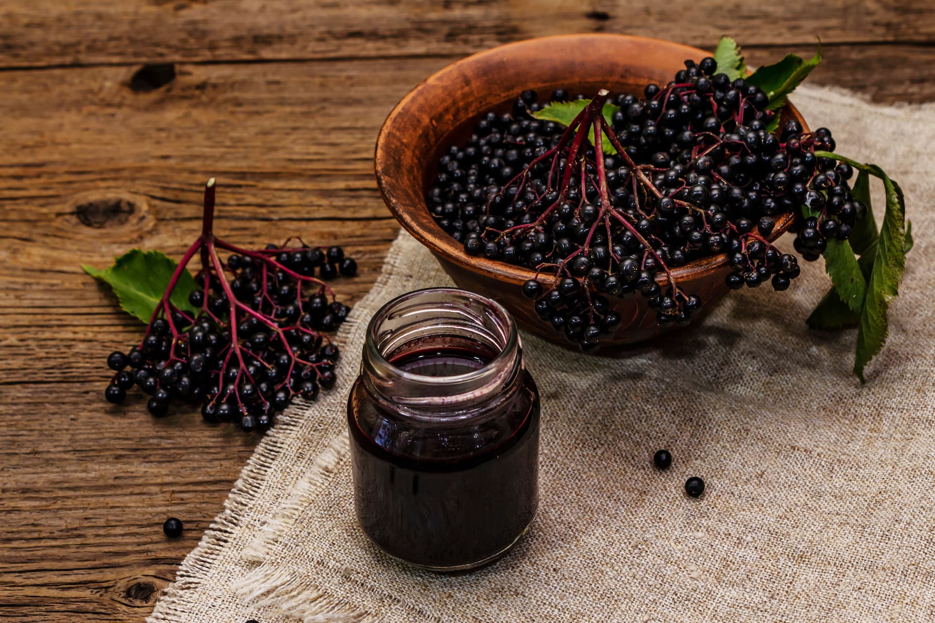 a jar of elderberry syrup on a table with some fresh elderberreis in a bowl