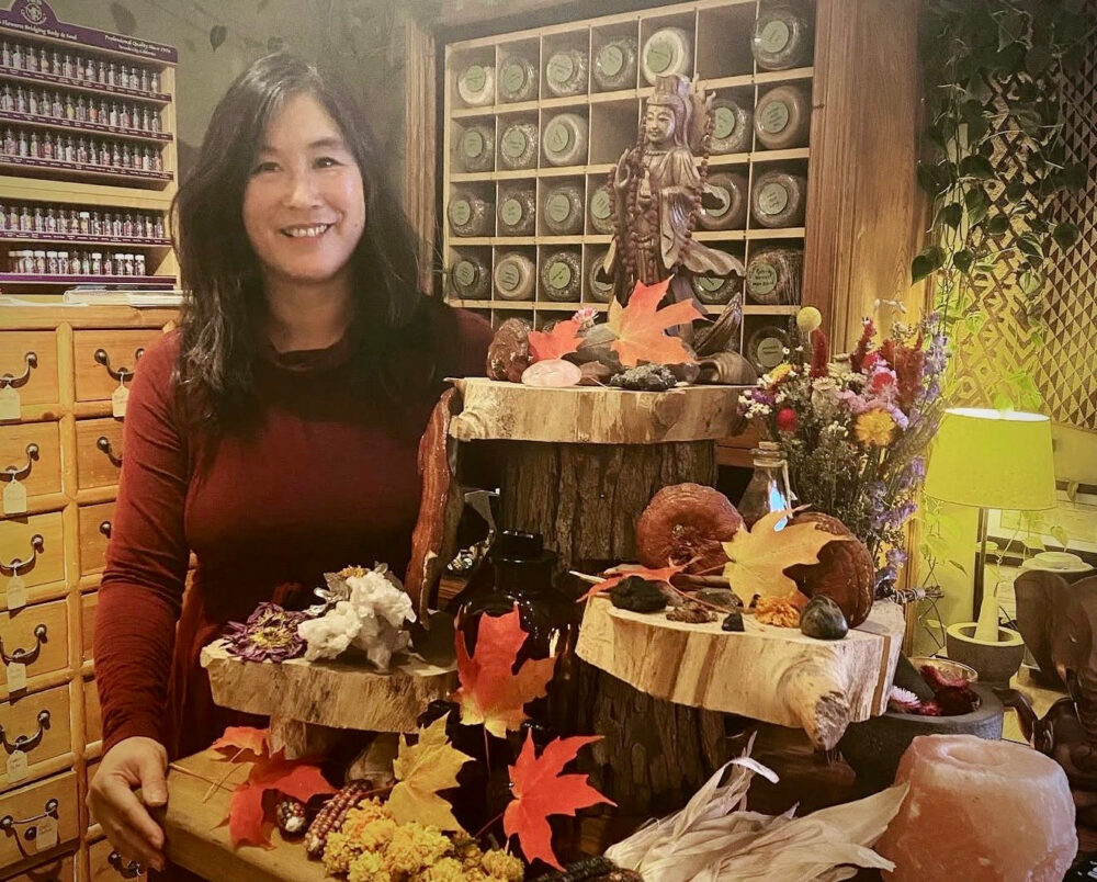 Herbalist standing in front of a fall altar with autumn leaves at an herbal apothecary shop.