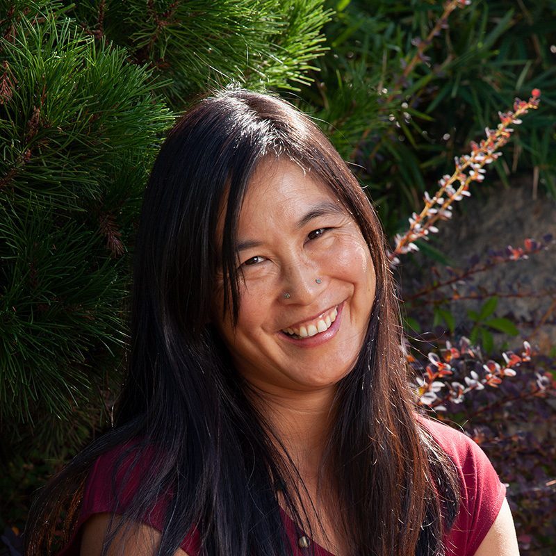 A woman smiling for the camera in front of some trees.