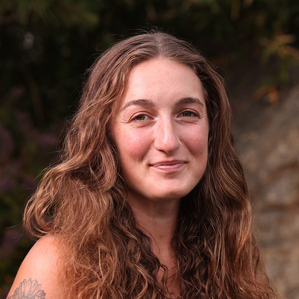 A woman with long hair and tattoos is smiling.